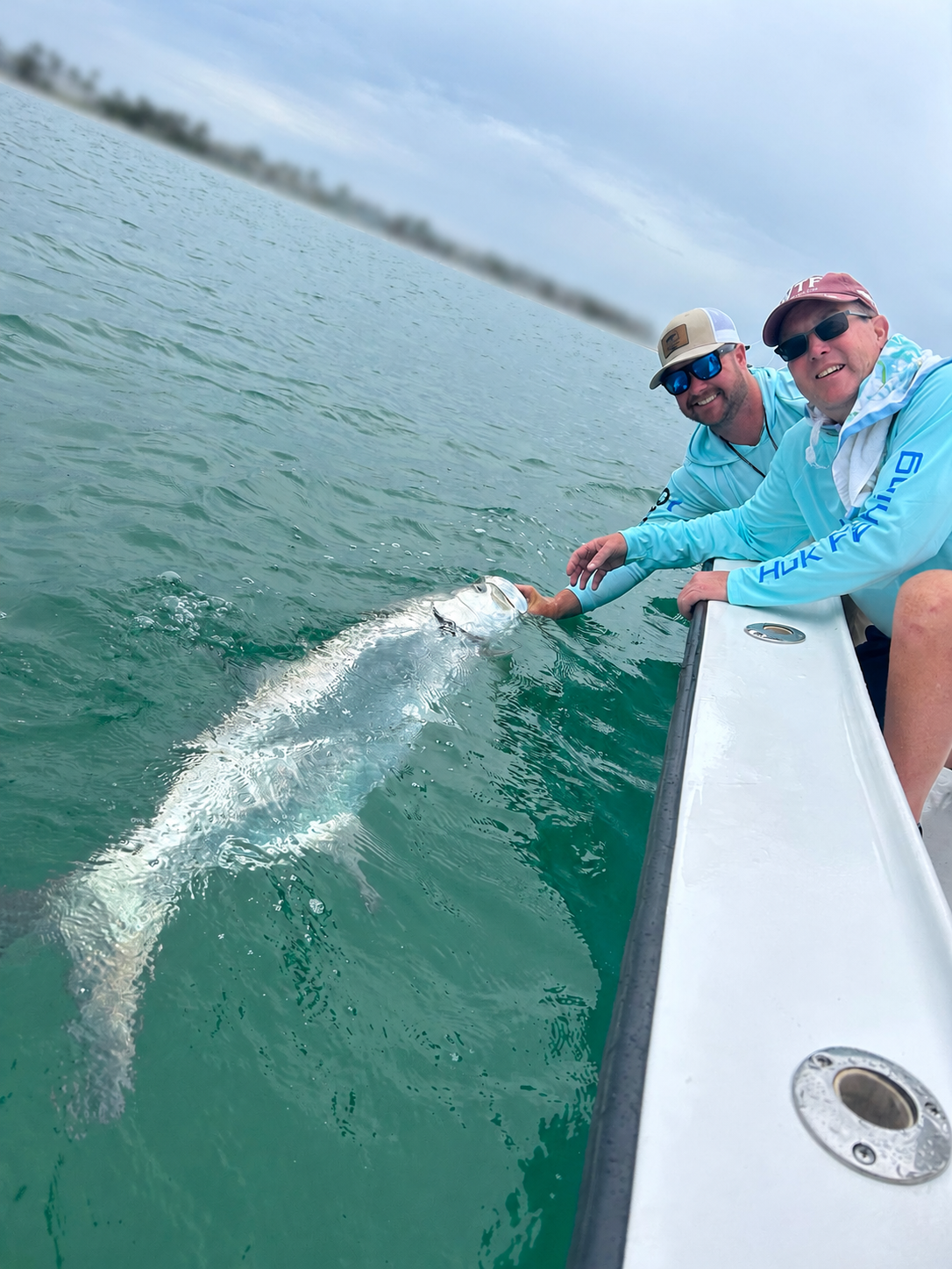 Two anglers with a tarpon at the gunwale of the charter boat