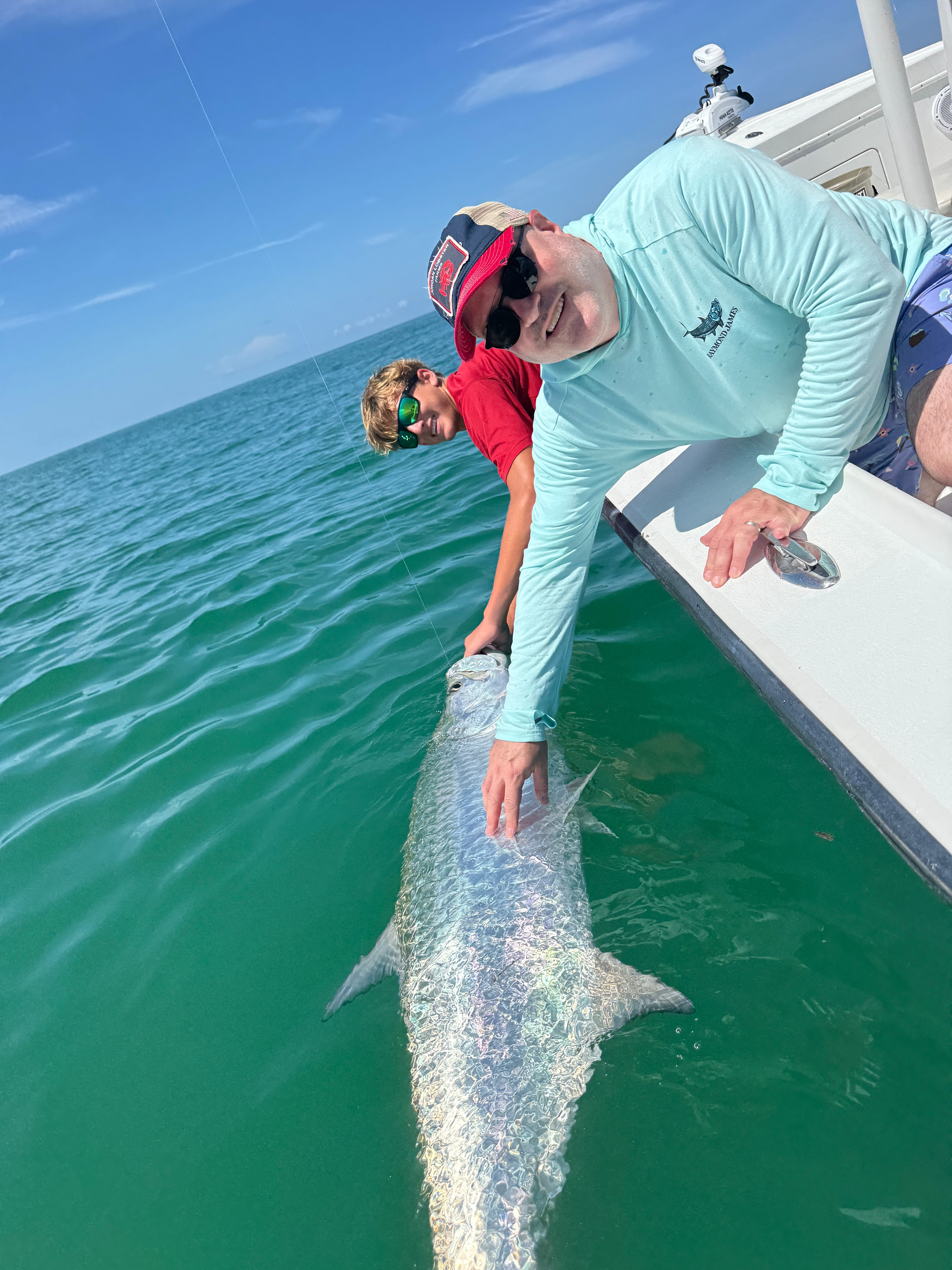 Group of young anglers with a massive tarpon alongside the boat